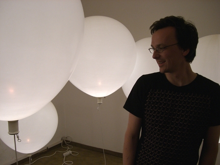 Tobias Kestel vom Designstudio White Elephant neben großen Luftballons, die Lampen mit Glühbirnen sind.